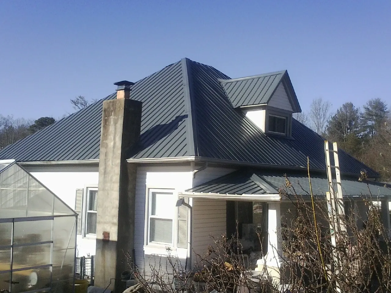 Dark blue standing seam metal roof on a white farmhouse with dormer — Slate & Tile Roof Repair by Roofing Brothers in Hall