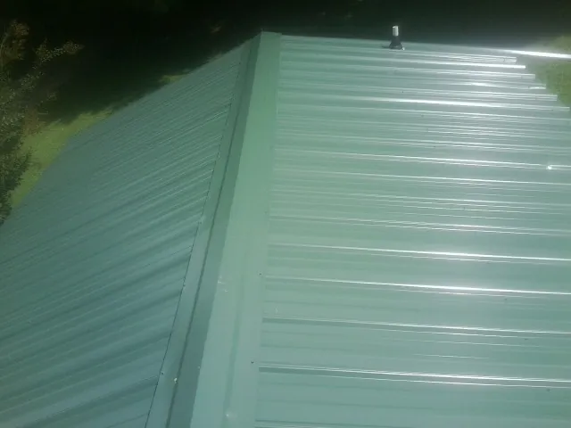 New green metal panels meeting at the ridge of a roof — Flat Roof Repair work by our crew in Hall