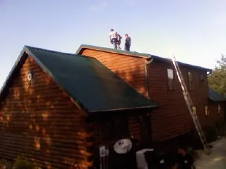 Crew on the ridge of a green metal roof on a two story log home in Hall