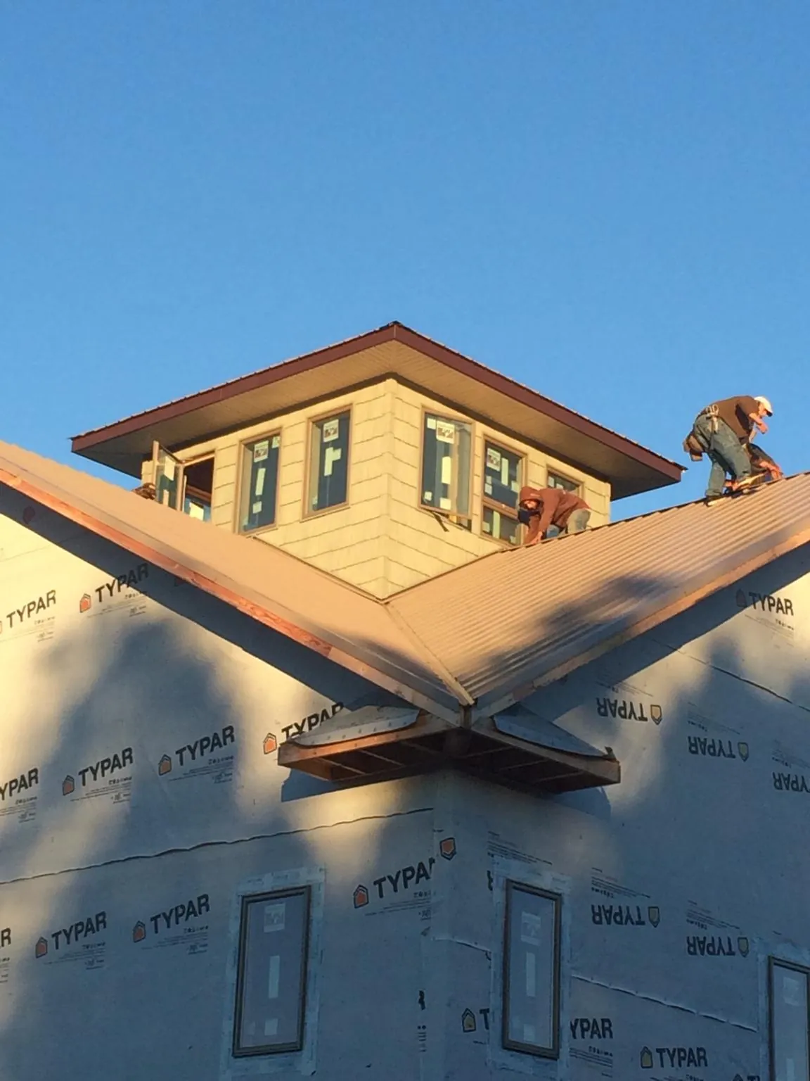 Roofers working around a rooftop cupola on a new metal roof at sunset — Roof Waterproofing in Hall by Roofing Brothers
